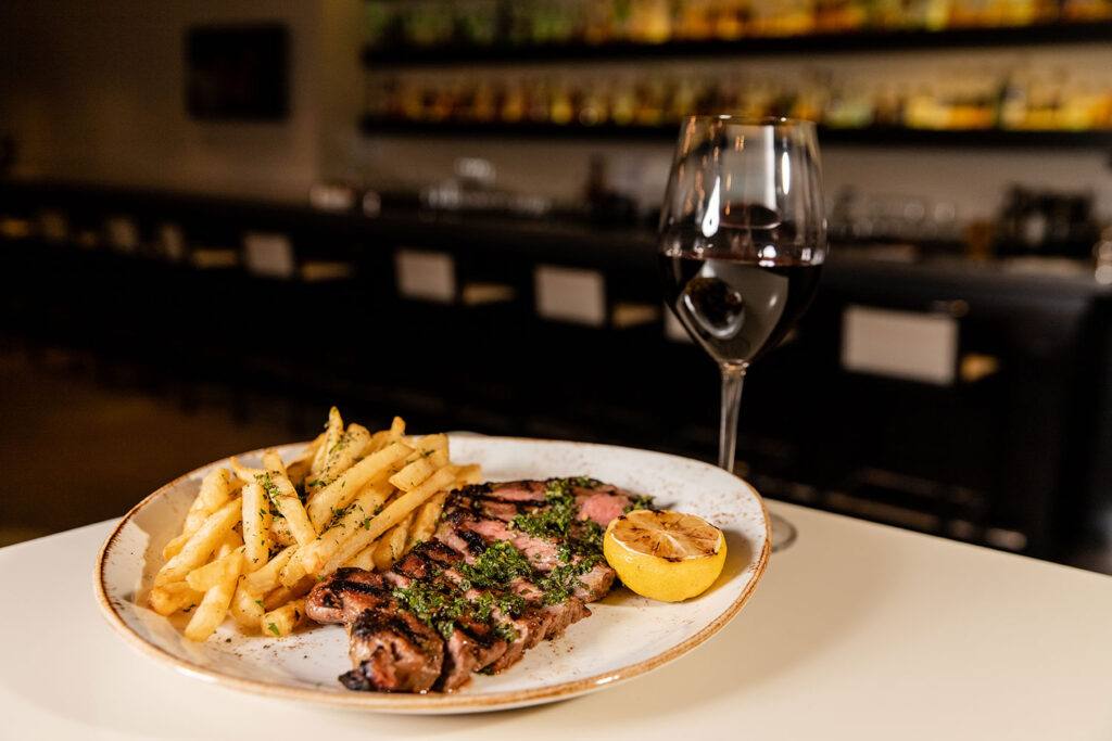 a white plate topped with steak and fries next to a glass of wine