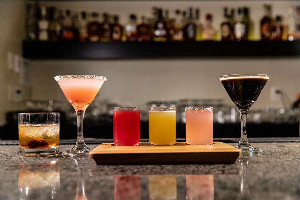 Six glasses of different types of drinks on a bar